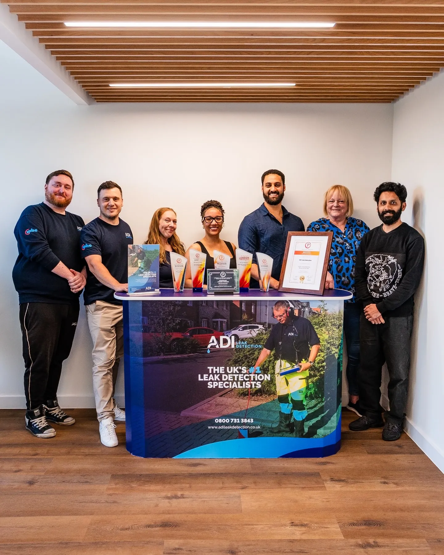 ADI team together at their office behind a display of company awards